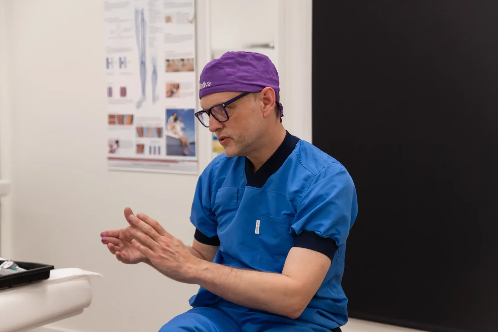 A male patient lying shirtless on a treatment bed wearing a disposable hair net, while a medical professional in a white lab coat and blue latex gloves applies a body sculpting device to his abdomen in a clinical setting.