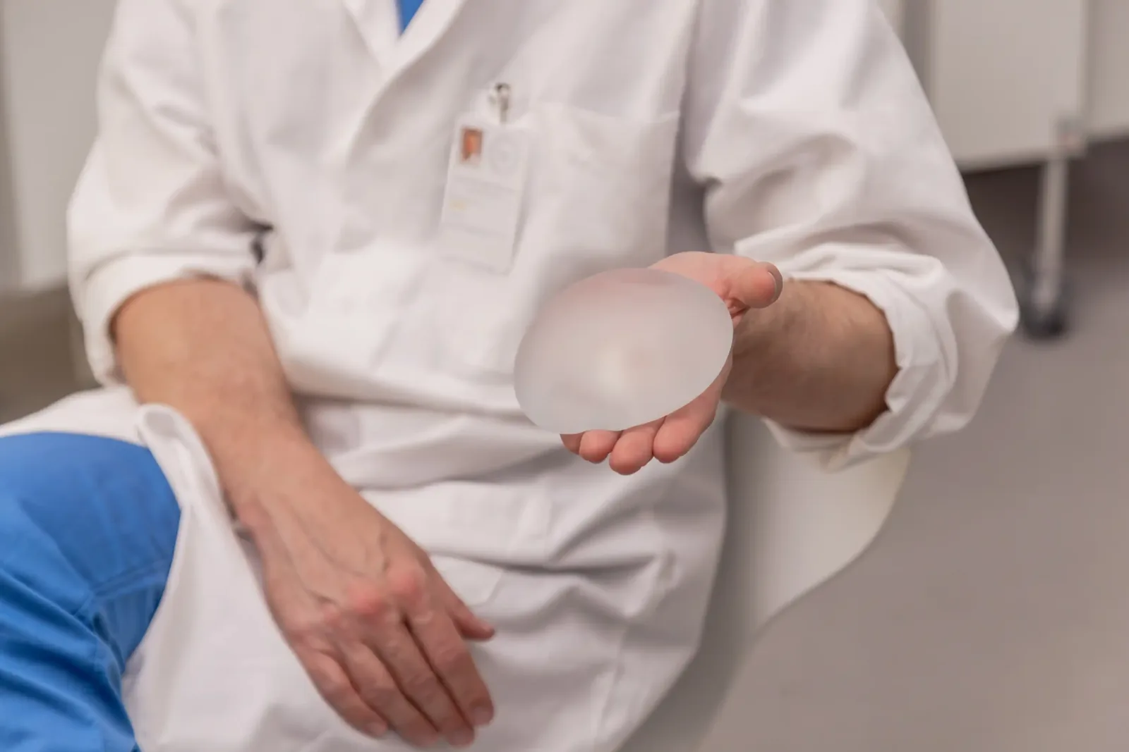 A male patient lying shirtless on a treatment bed wearing a disposable hair net, while a medical professional in a white lab coat and blue latex gloves applies a body sculpting device to his abdomen in a clinical setting.