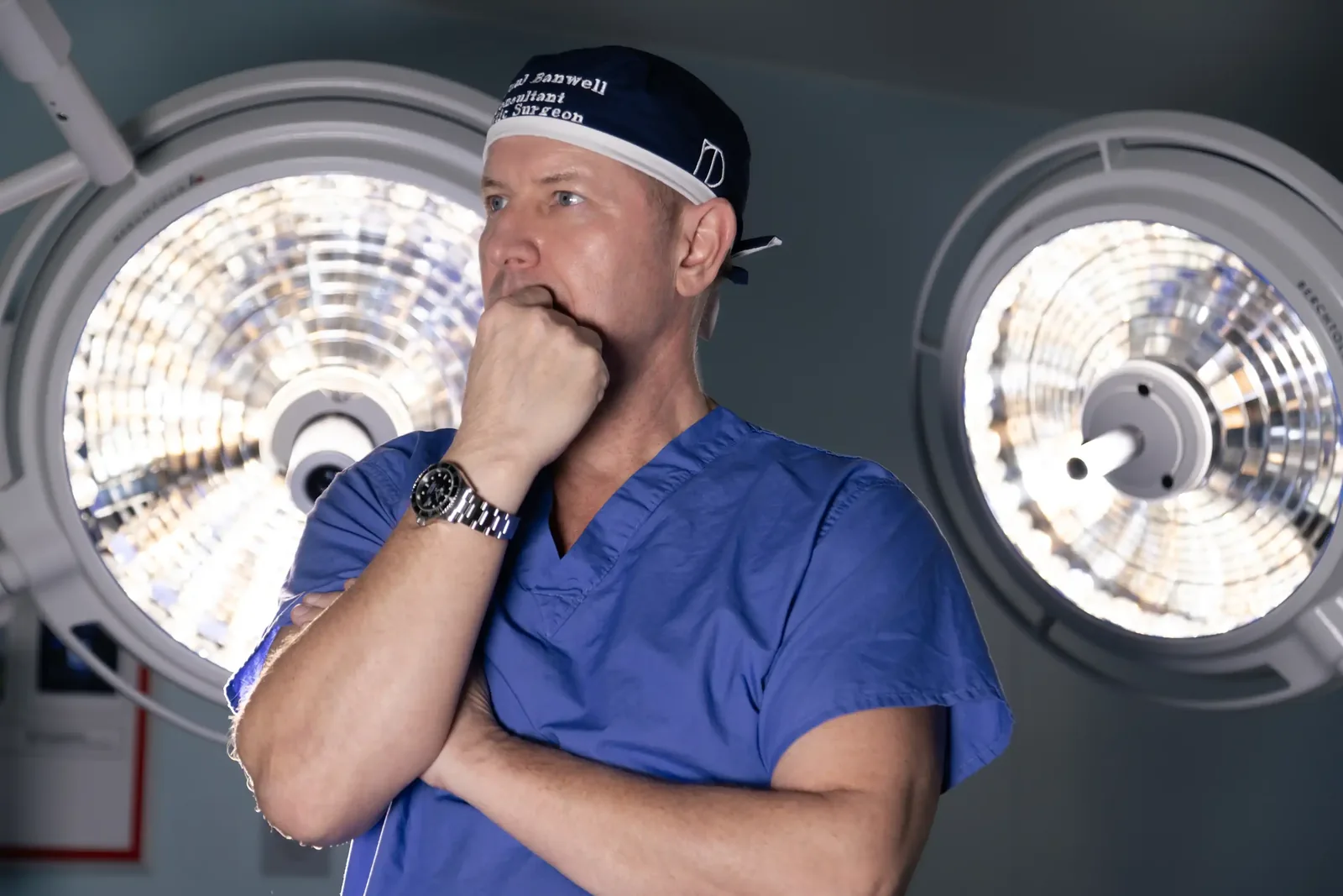 A male patient lying shirtless on a treatment bed wearing a disposable hair net, while a medical professional in a white lab coat and blue latex gloves applies a body sculpting device to his abdomen in a clinical setting.