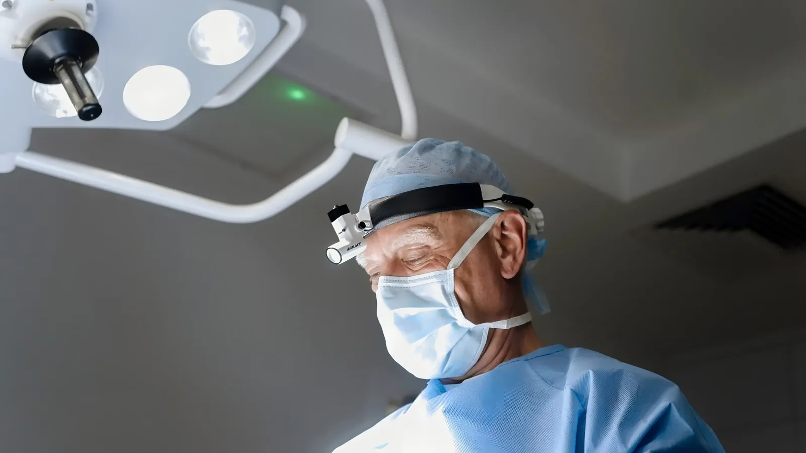 A male patient lying shirtless on a treatment bed wearing a disposable hair net, while a medical professional in a white lab coat and blue latex gloves applies a body sculpting device to his abdomen in a clinical setting.