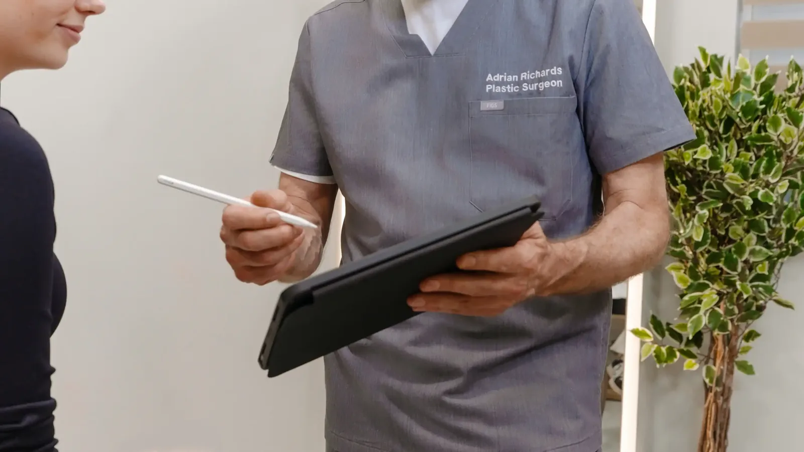 A male patient lying shirtless on a treatment bed wearing a disposable hair net, while a medical professional in a white lab coat and blue latex gloves applies a body sculpting device to his abdomen in a clinical setting.