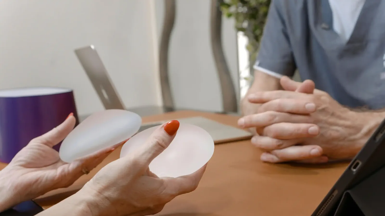A male patient lying shirtless on a treatment bed wearing a disposable hair net, while a medical professional in a white lab coat and blue latex gloves applies a body sculpting device to his abdomen in a clinical setting.