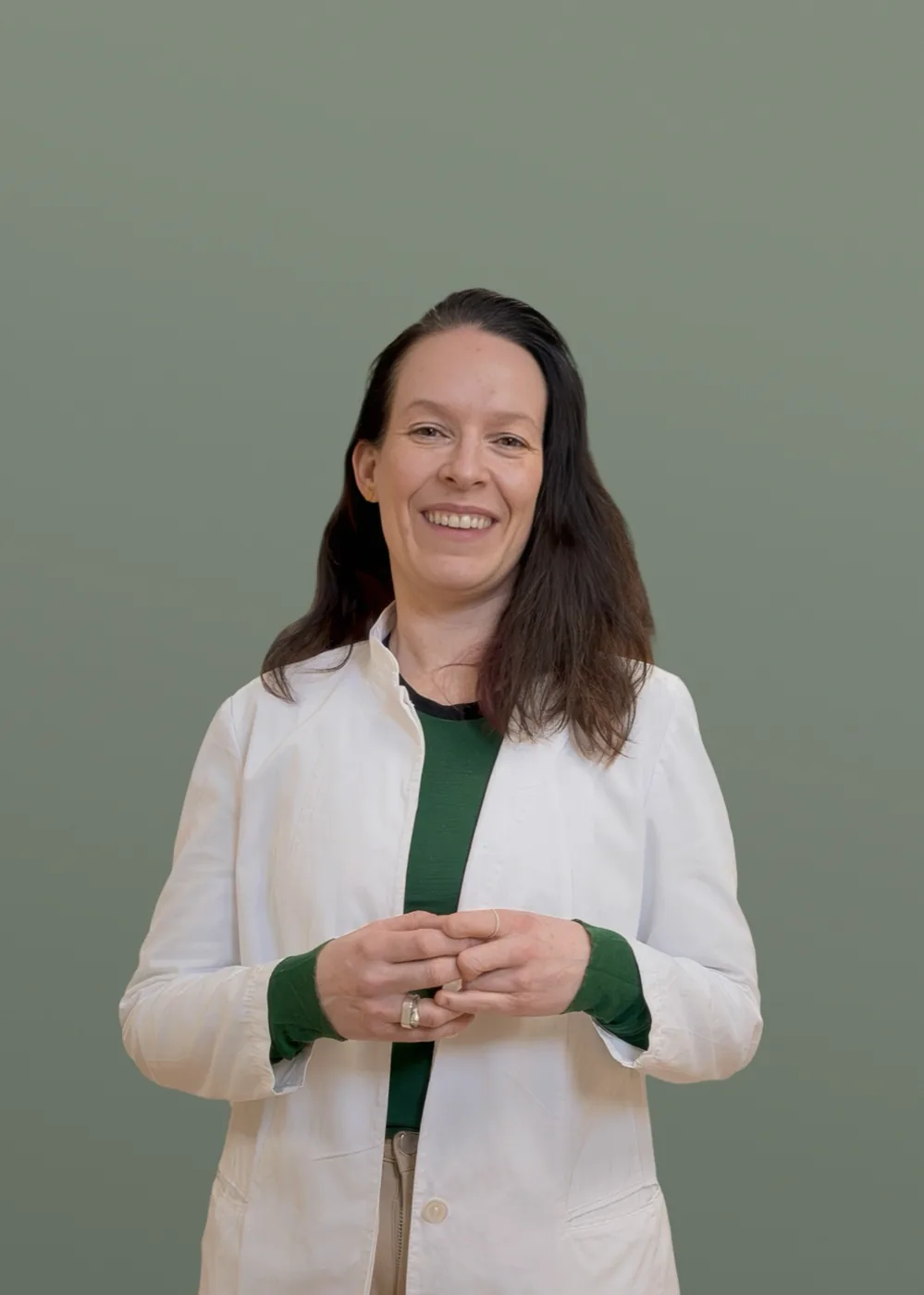 Dr. Iselin Saltvig, a smiling woman with long dark hair, wearing a white lab coat over a green top, with her hands gently clasped in front of her.