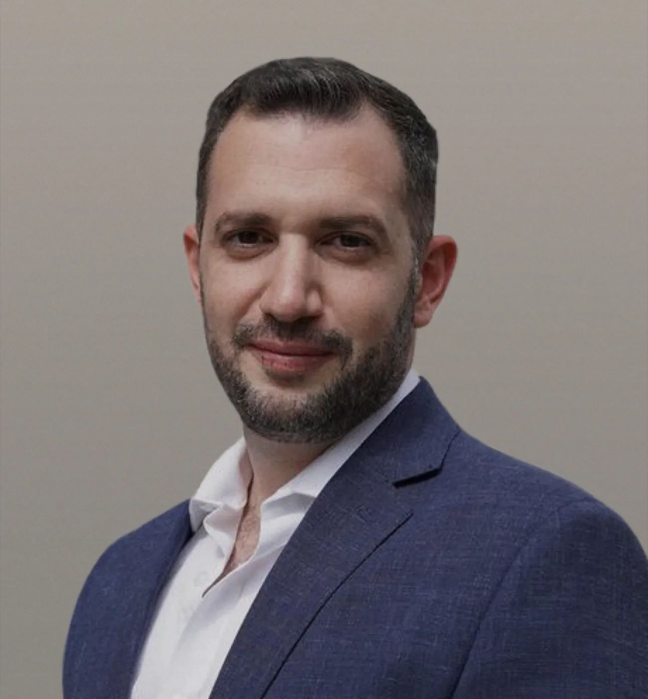 Professional headshot of Mr. Ali Arnaout, a man with short dark hair and a trimmed beard, wearing a navy blue blazer over an open-collar white dress shirt, smiling slightly toward the camera.