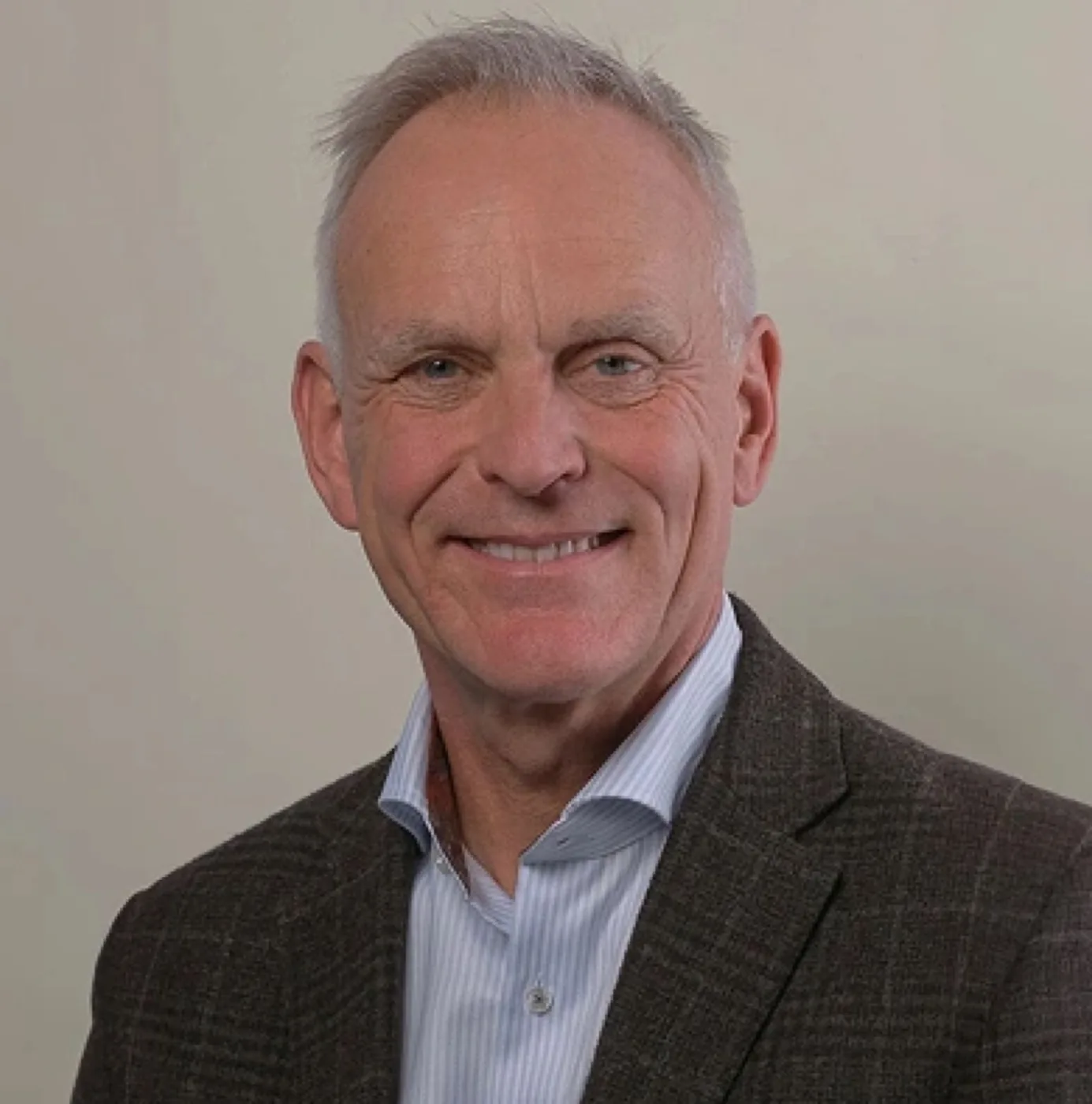 Professional headshot of Mr. Adrian Richards, a middle-aged man with short gray hair and blue eyes, smiling warmly, wearing a light blue striped shirt and a brown plaid blazer.