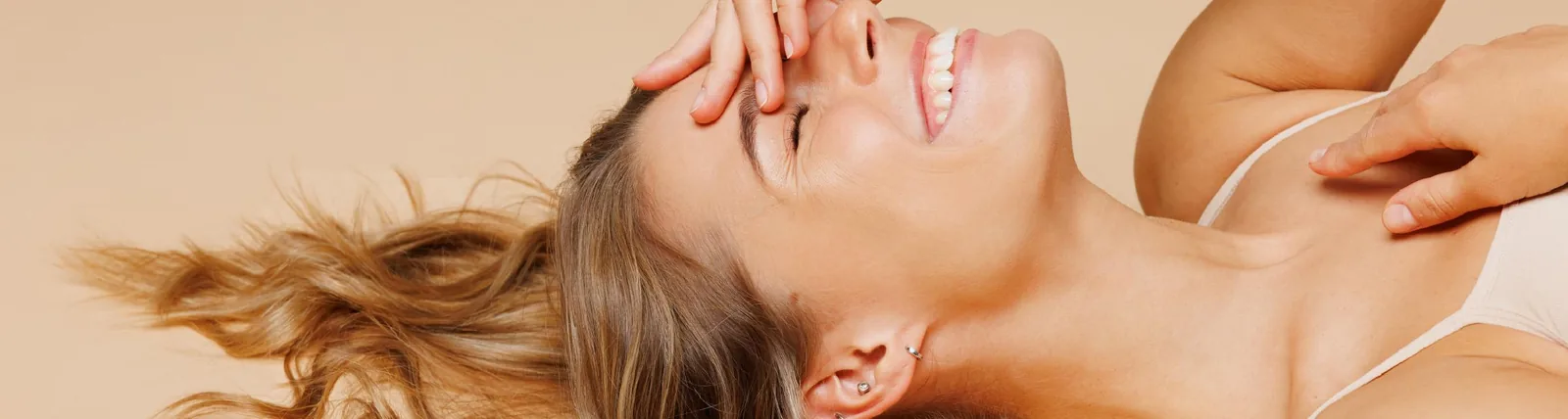 A smiling woman with blonde hair lying back, touching her face and neck, appearing relaxed and joyful, in the context of body contouring results.