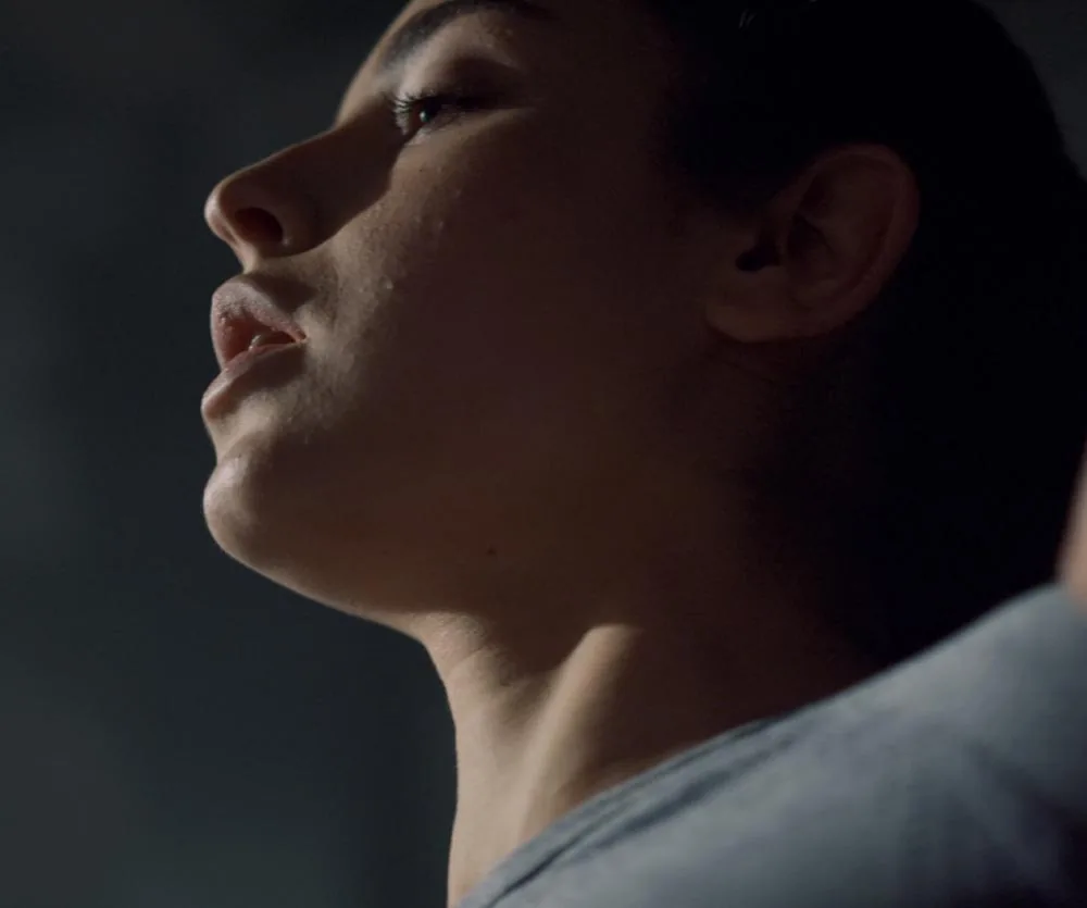 Close-up side profile of a person tilting their head upward, with visible sweat or moisture on the skin around the chin and jaw area, wearing a light gray top, illustrating the neck and jawline — relevant to neck lift scars context.