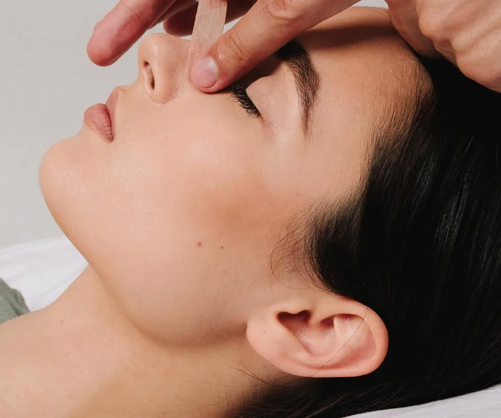 A woman lying on her back with eyes closed while a practitioner applies gentle pressure to the bridge of her nose with their fingers, illustrating a septoplasty recovery or nasal treatment procedure.