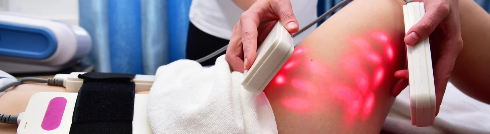 A healthcare professional applying Lipo-Light body contouring treatment to a patient's thigh, using two handheld LED light therapy pads emitting red light, with a black electrode strap also attached to the body, in a clinical setting.