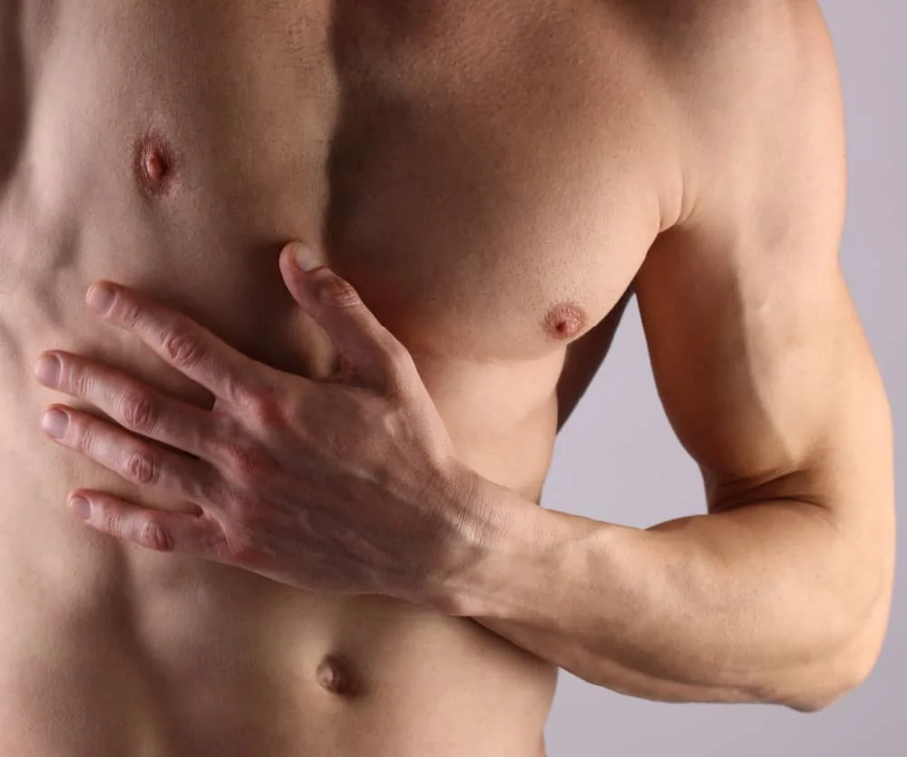 A shirtless muscular man pressing his hand against his chest, illustrating a topic related to laser hair removal on the male torso.