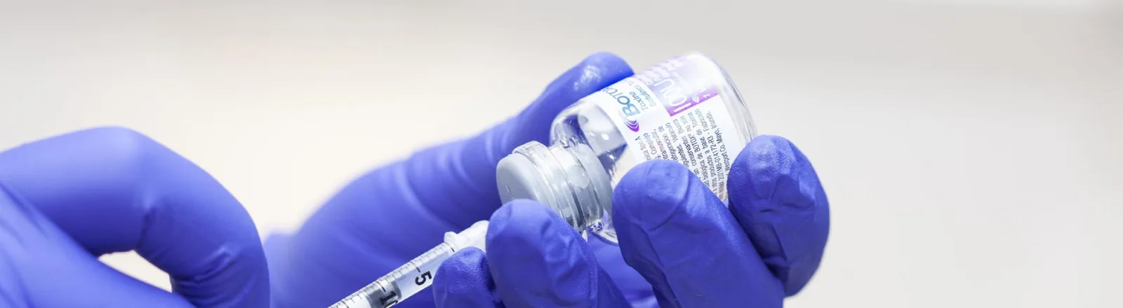 A gloved healthcare professional wearing blue latex gloves drawing Botox from a small glass vial into a syringe, following manufacturer guidelines for preparation.