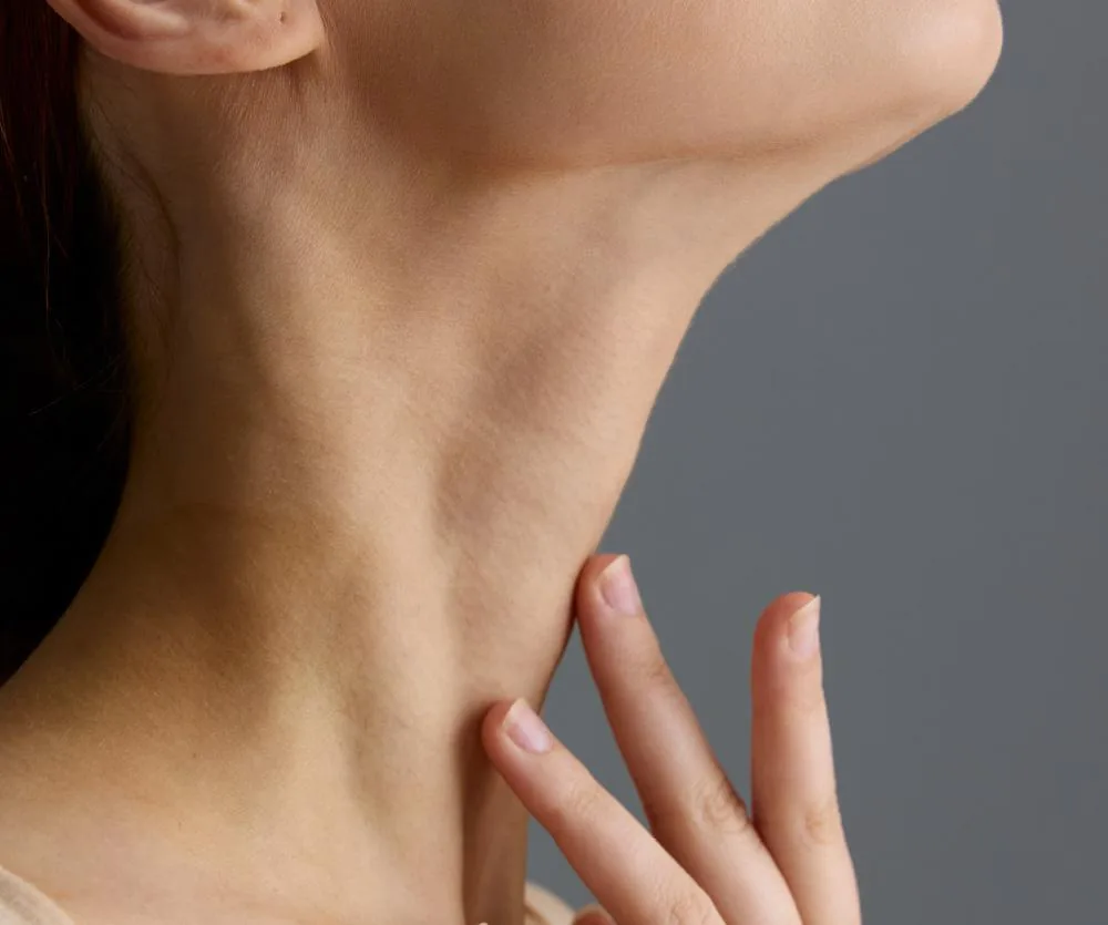Close-up side profile of a woman's neck and jawline, with her hand gently resting at the base of her throat, showcasing smooth skin — illustrating a neck lift procedure.