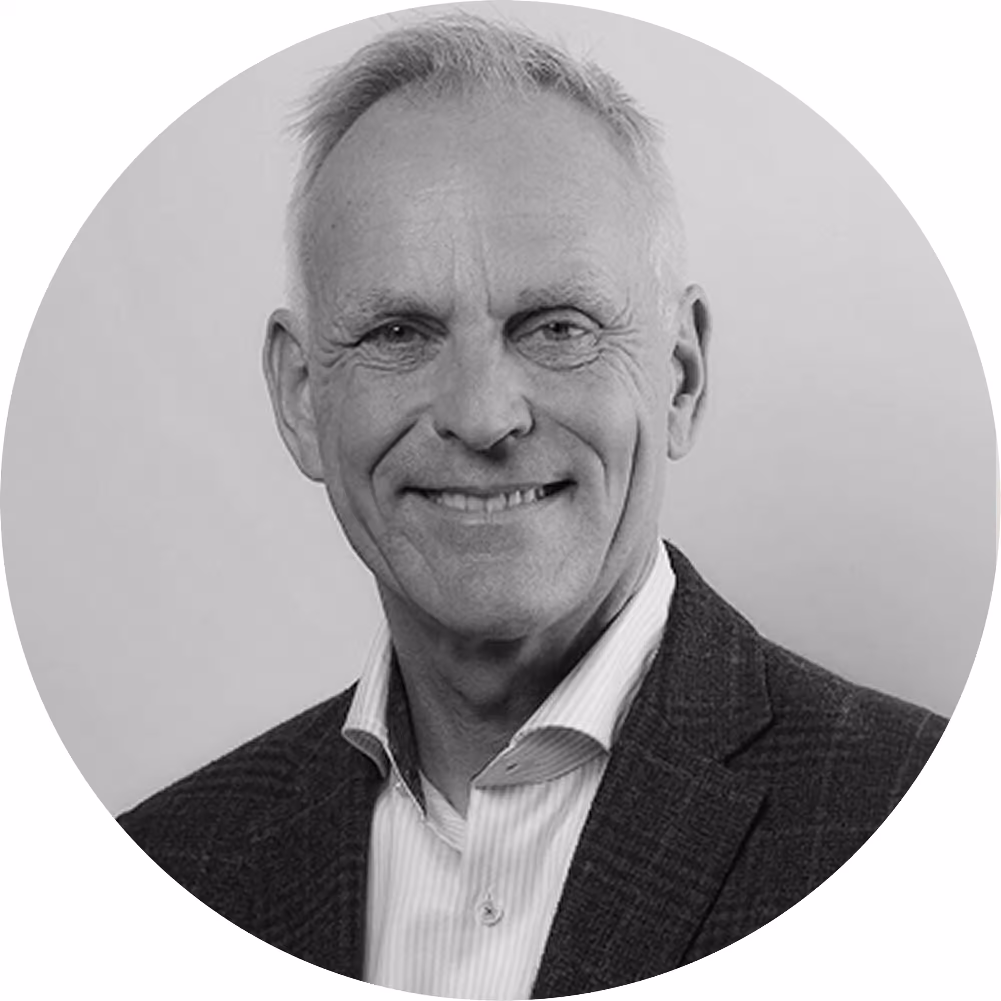 Black and white circular portrait photo of a smiling middle-aged man with short gray hair, wearing a dark blazer over an open-collar striped shirt.