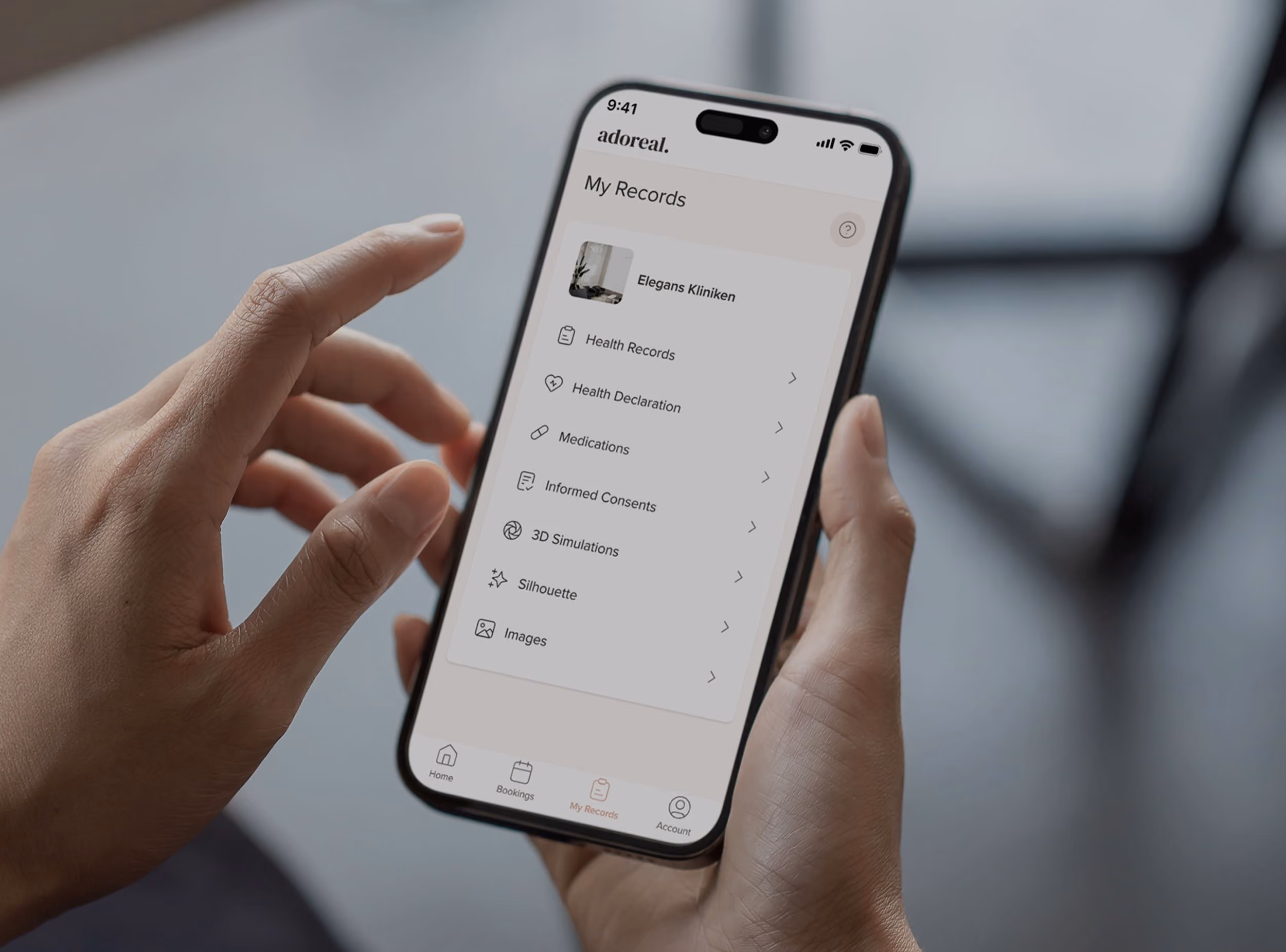 A person holding a smartphone in both hands, displaying the 'adoreal.' mobile app's 'My Records' screen, which lists menu items including Health Records, Health Declaration, Medications, Informed Consents, 3D Simulations, Silhouette, and Images, under a