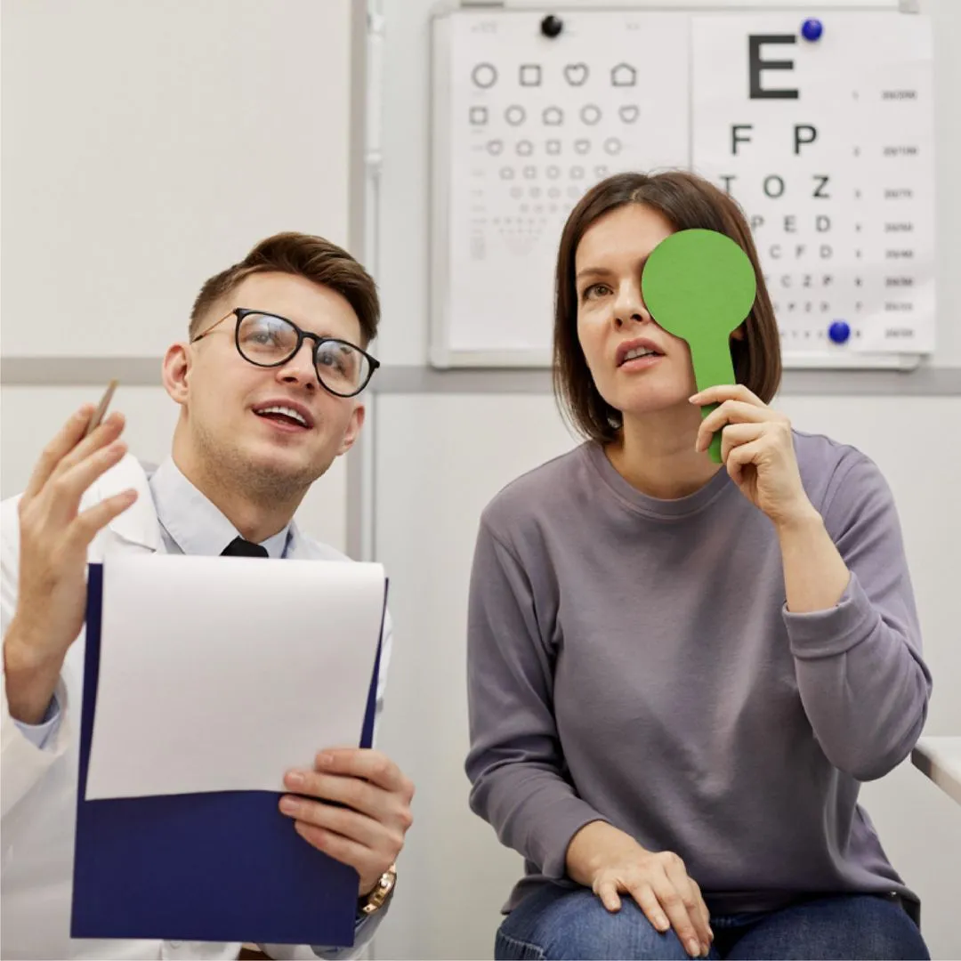 Optometrist with clipboard explaining eye test to woman covering one eye with green paddle.