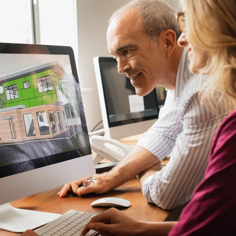Man and woman reviewing 3D house design rendering on a computer in an office.
