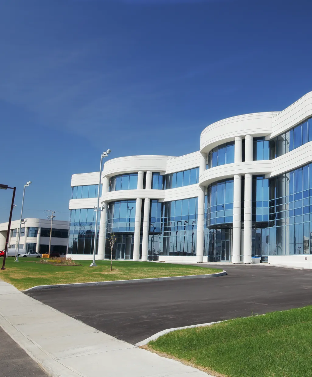 Modern office building with white curved columns and blue reflective glass windows under a clear sky.