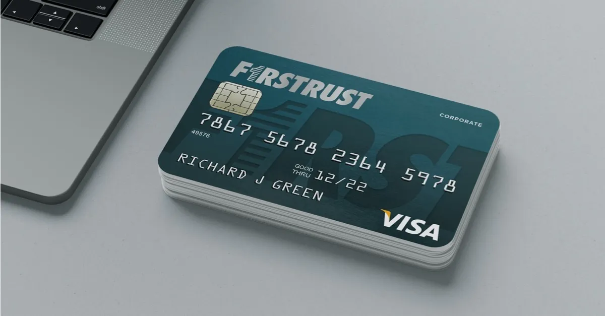 Stack of FirstTrust corporate Visa cards on a table near a laptop keyboard.