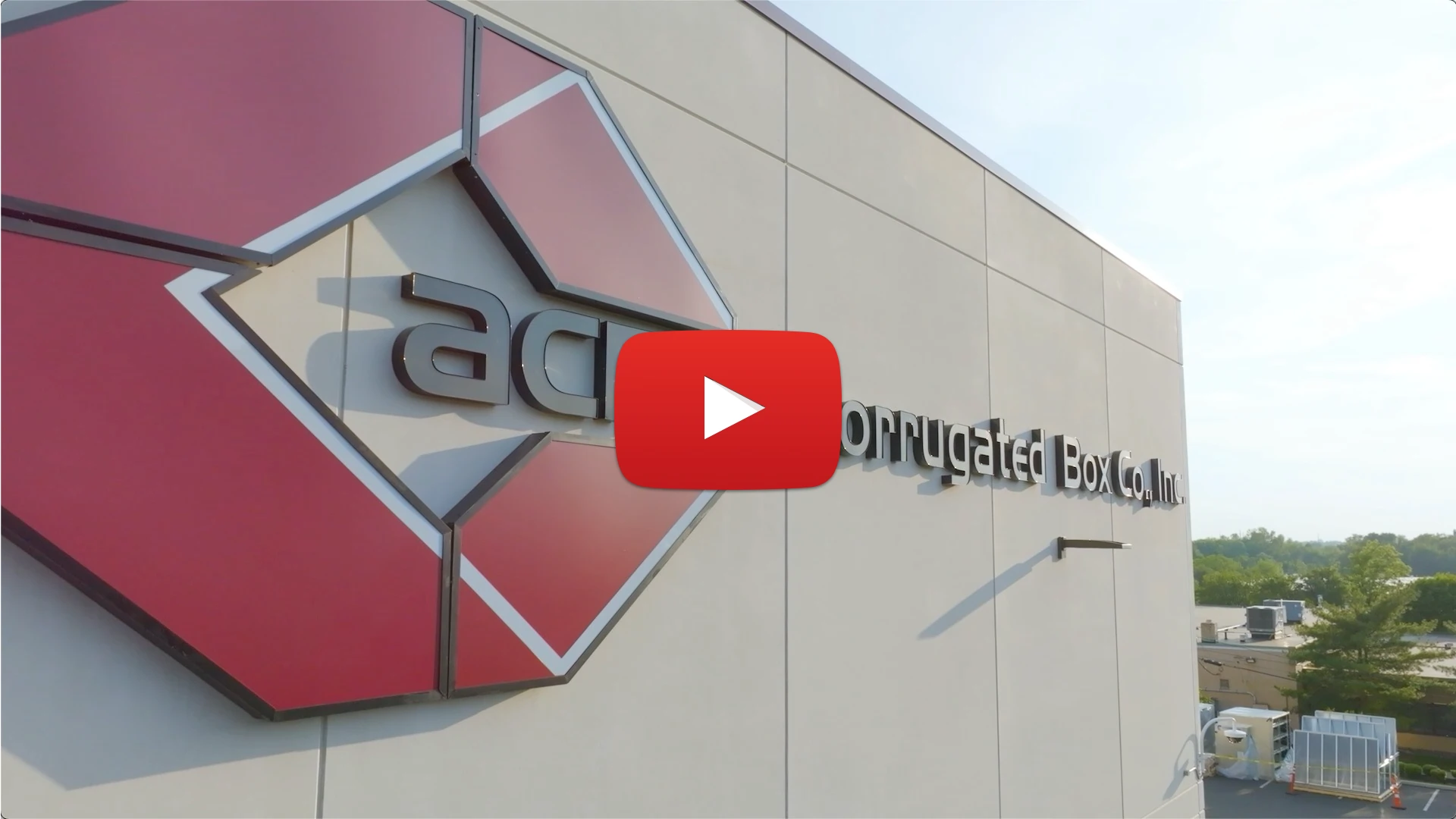 Exterior wall of a building with a large red geometric logo and text reading Acme Corrugated Box Co.