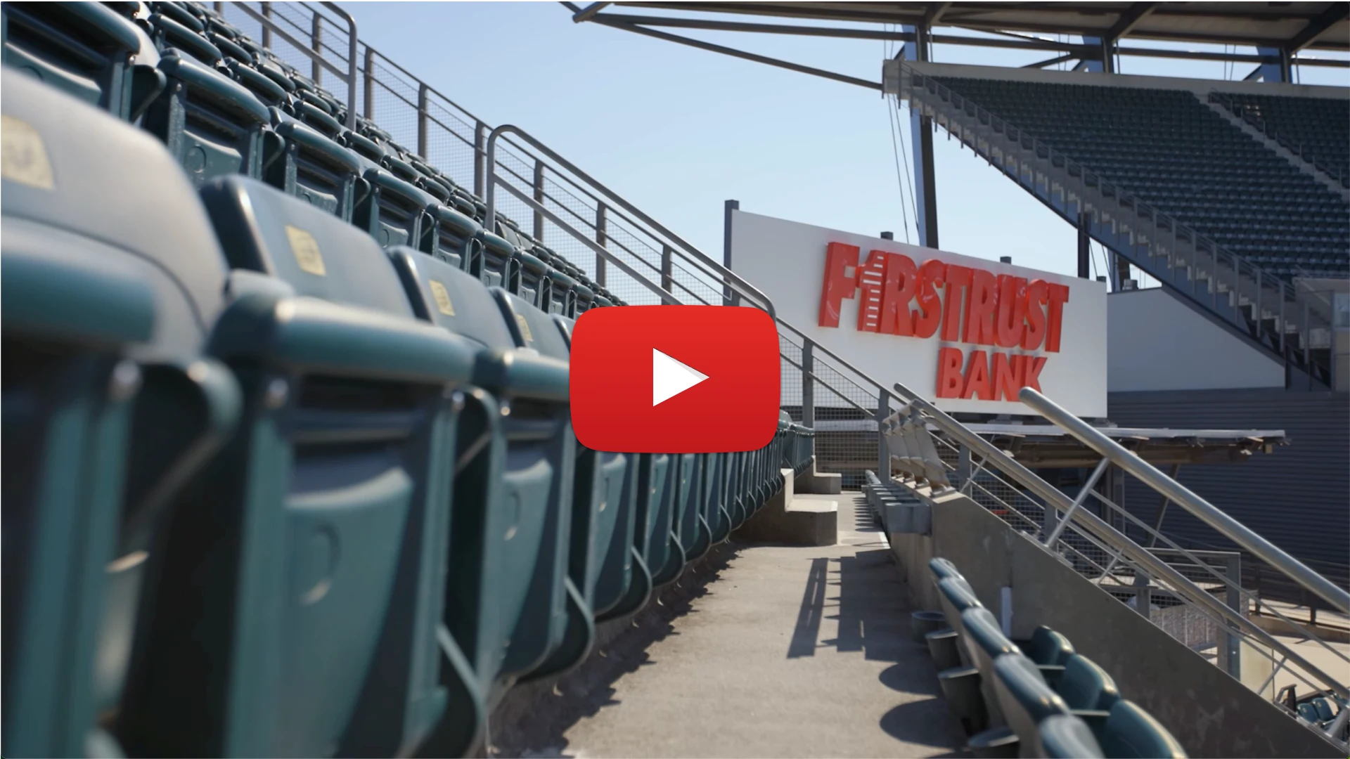 Empty stadium seating with First Trust Bank sign visible on the right side in daylight.