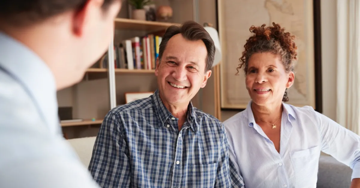 Smiling middle-aged couple consulting a professional in a cozy, book-filled office setting.