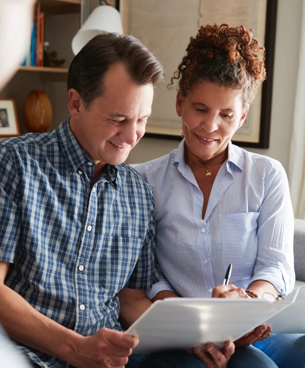 Smiling middle-aged man and woman reviewing papers together in a cozy home setting.