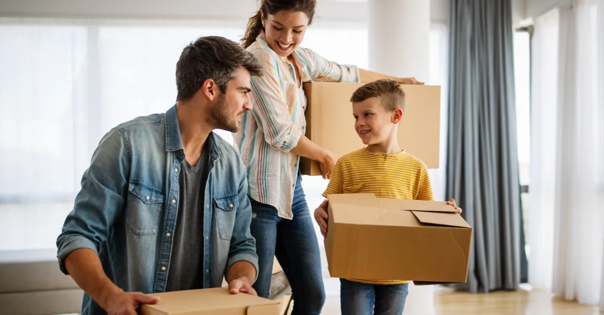Happy family carrying cardboard boxes inside a bright home, appearing to be moving or unpacking.