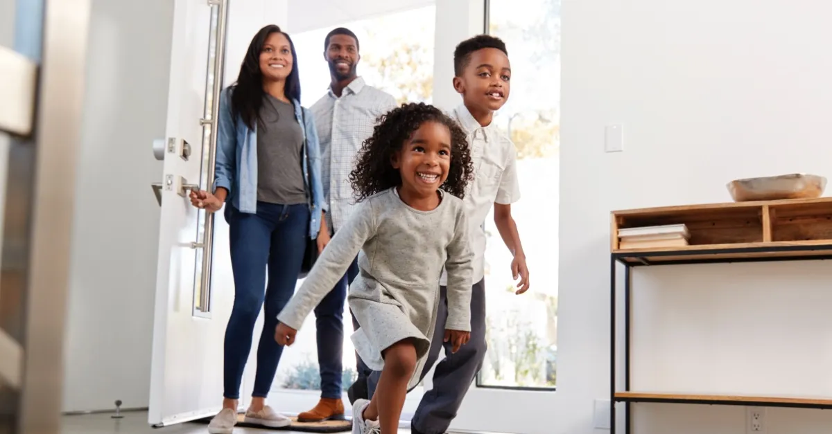 Smiling family of four entering their home with children excitedly running inside.