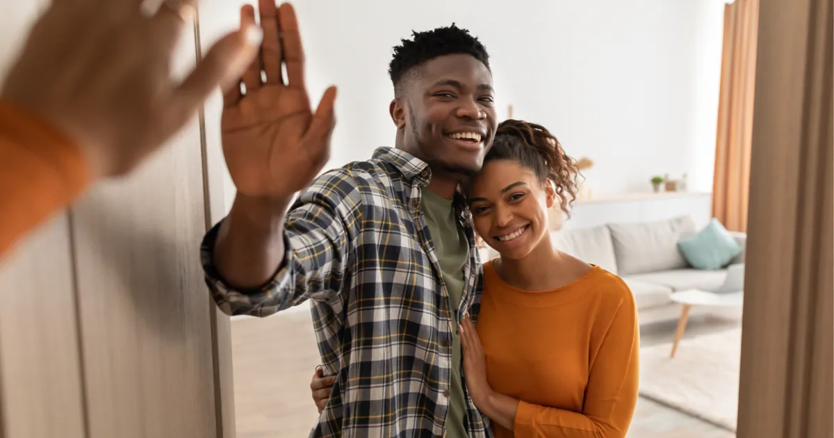 Smiling couple welcomes with a high-five at the entrance of a bright living room.