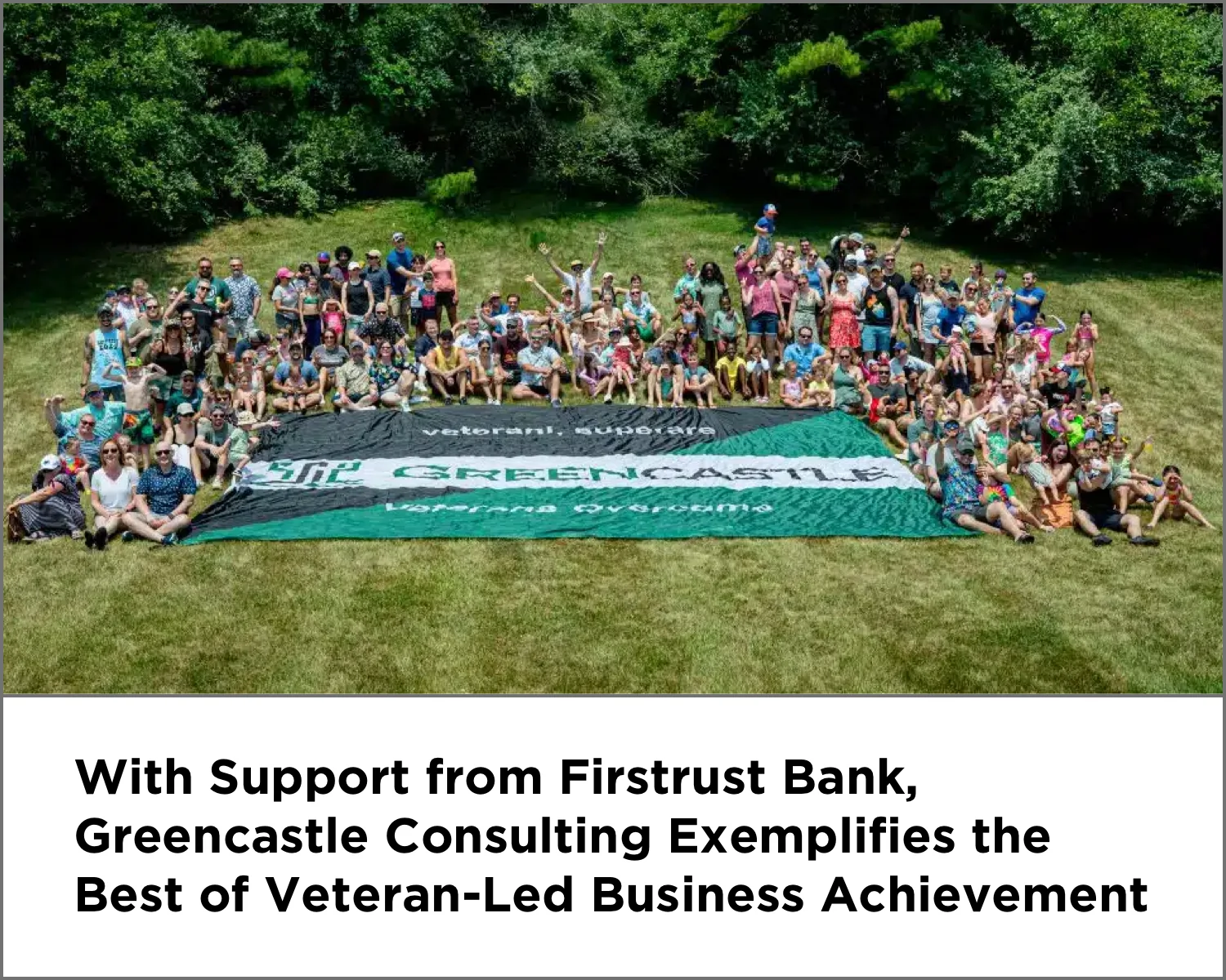 Large group of people posing outdoors behind a Greencastle banner on grass with trees in the background.