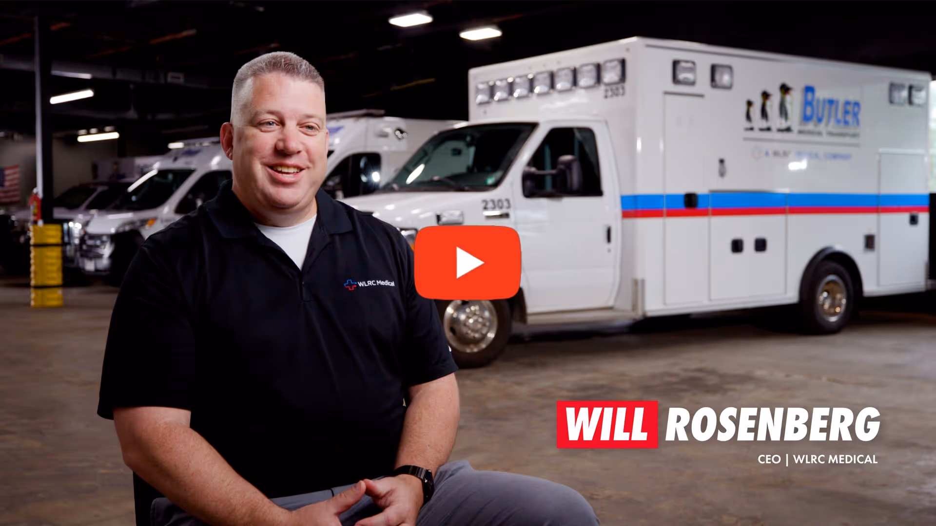 Man in black polo with WLRC Medical logo seated in front of ambulances inside a garage.