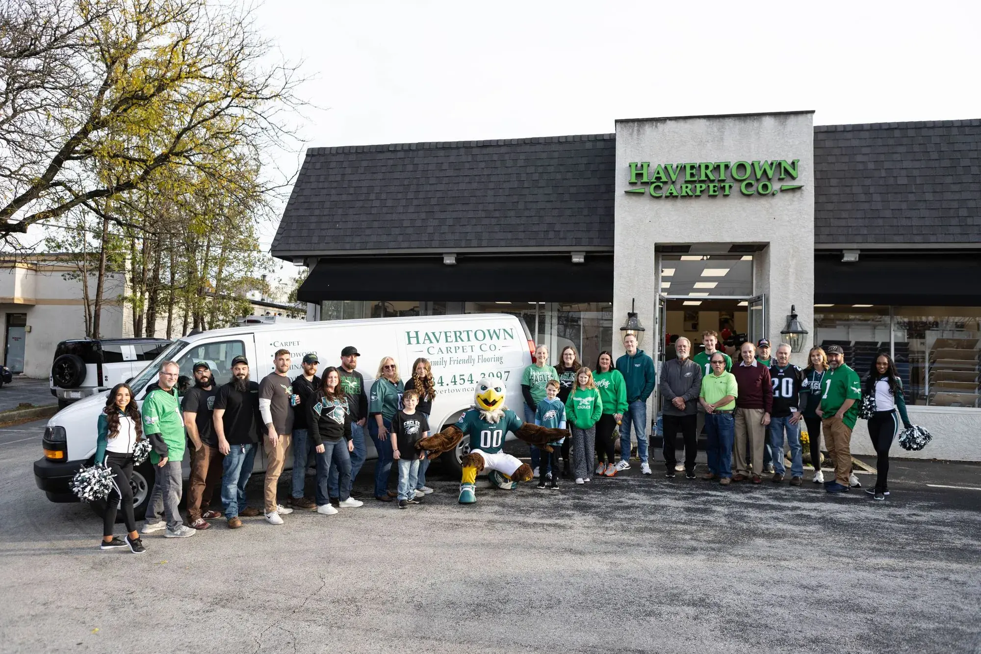 Group of people and an eagle mascot outside Havertown Carpet Co. building next to a company van.