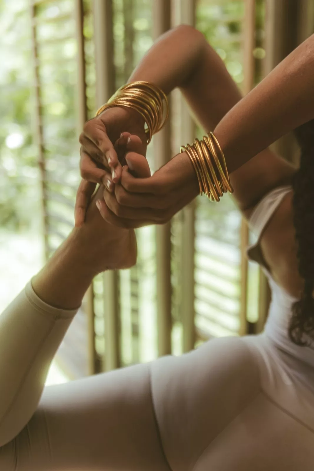 Close-up of a person with golden bangles practicing an advanced yoga stretch inside The Shaba Shala studio.