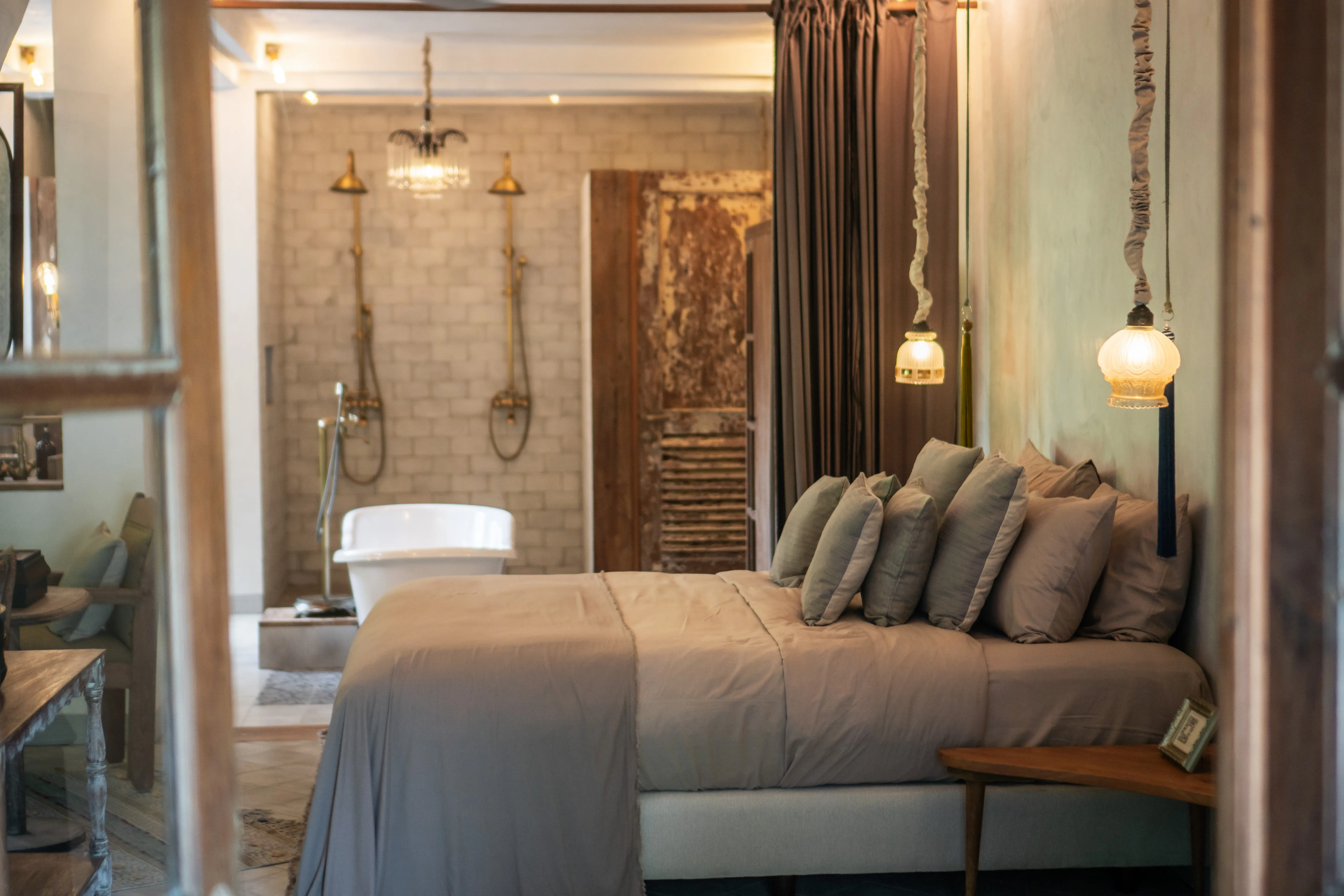 Luxury hotel suite featuring an open-concept bedroom leading into a bathroom with a freestanding bathtub and dual brass showers