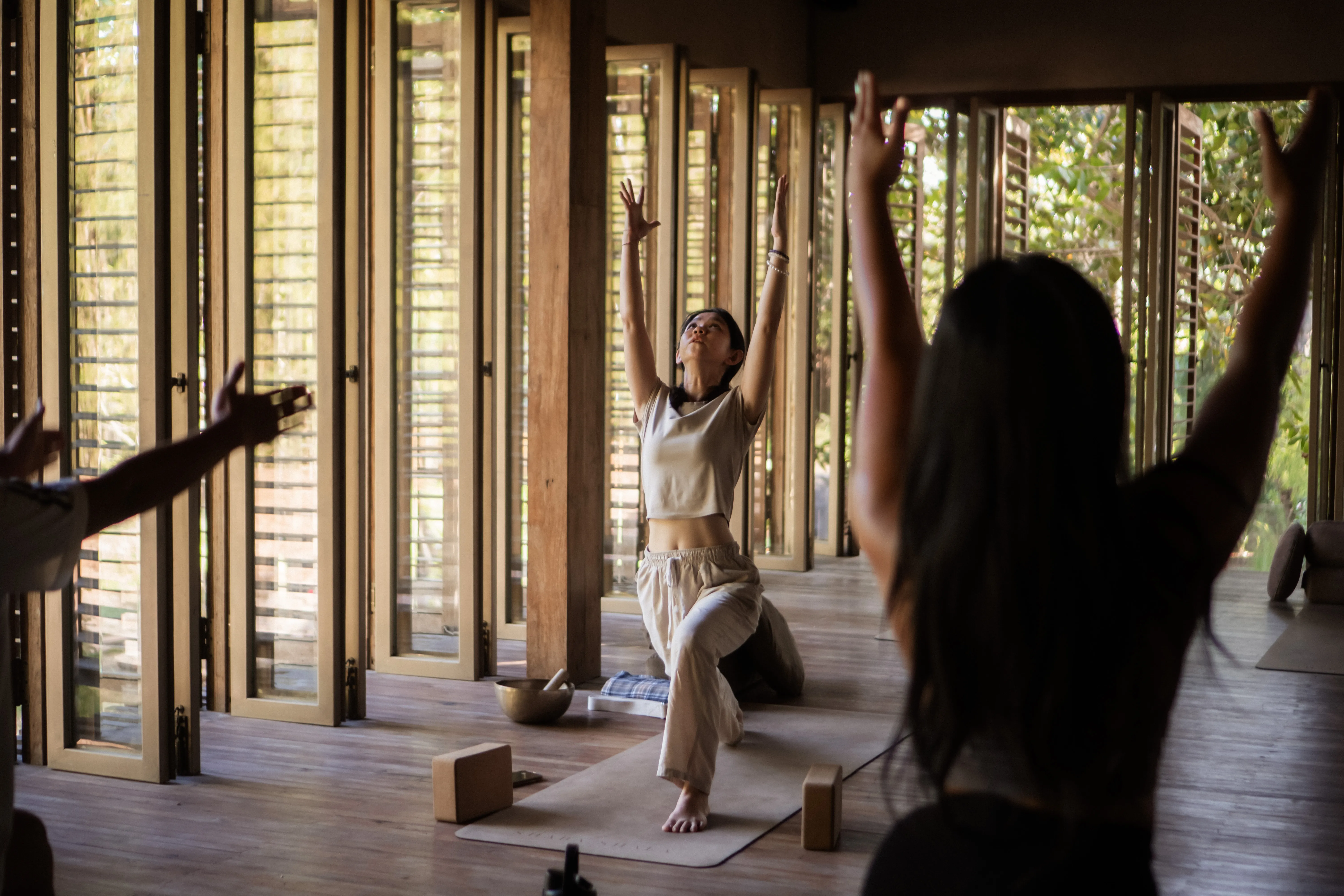 Participants raising their arms into High Lunge pose during a group Vinyasa Yoga flow session at The Shaba Shala.