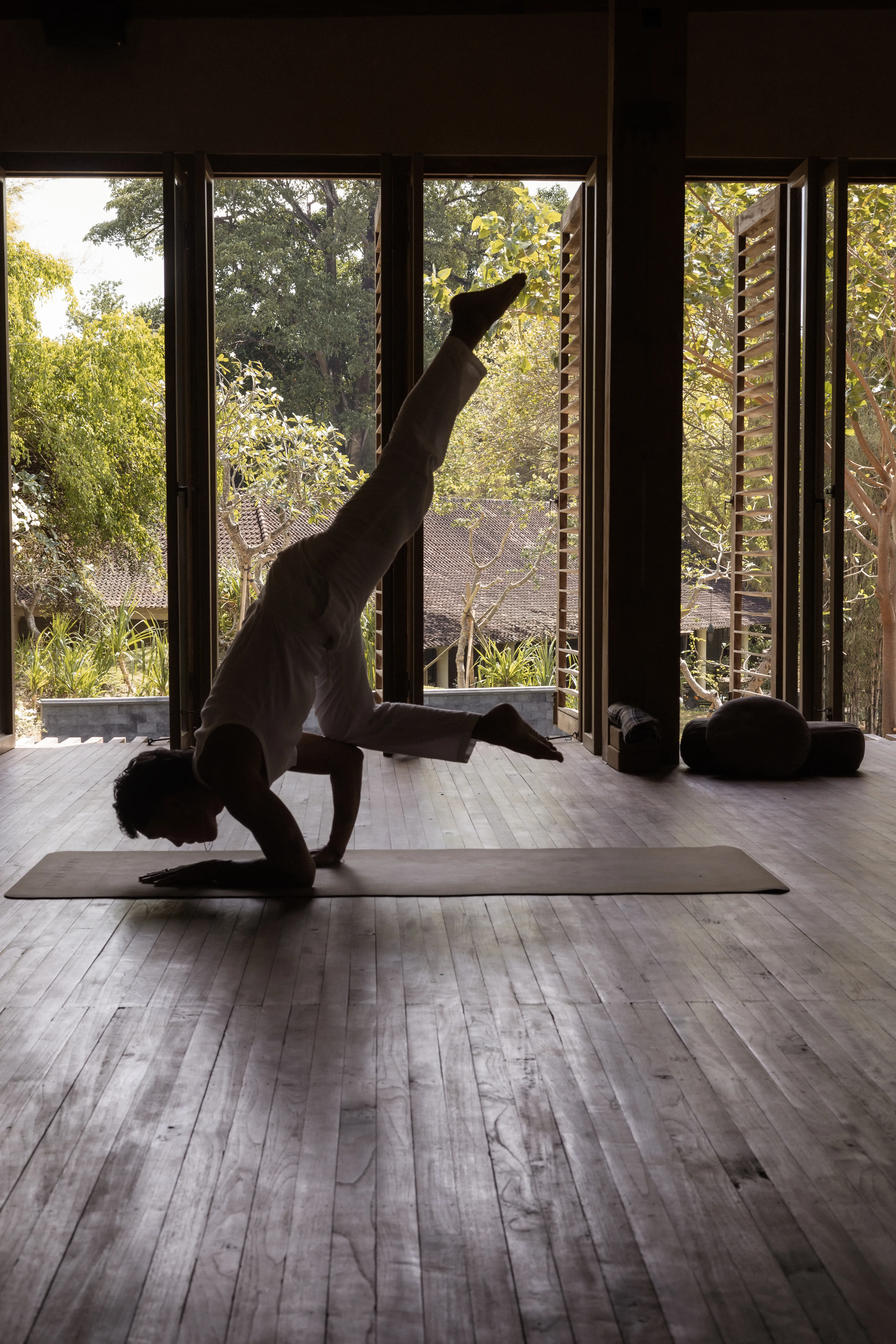 A male instructor demonstrating an advanced forearm balance yoga pose on a mat inside the wooden studio at Shaba Shala.