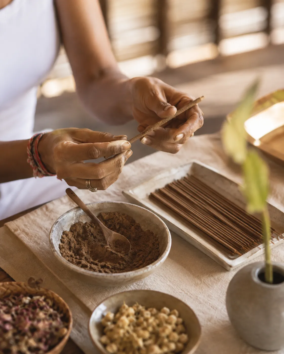 A beautifully organized workshop table featuring bowls of aromatic herbal powders, dried flowers, and hand-rolled incense sticks.