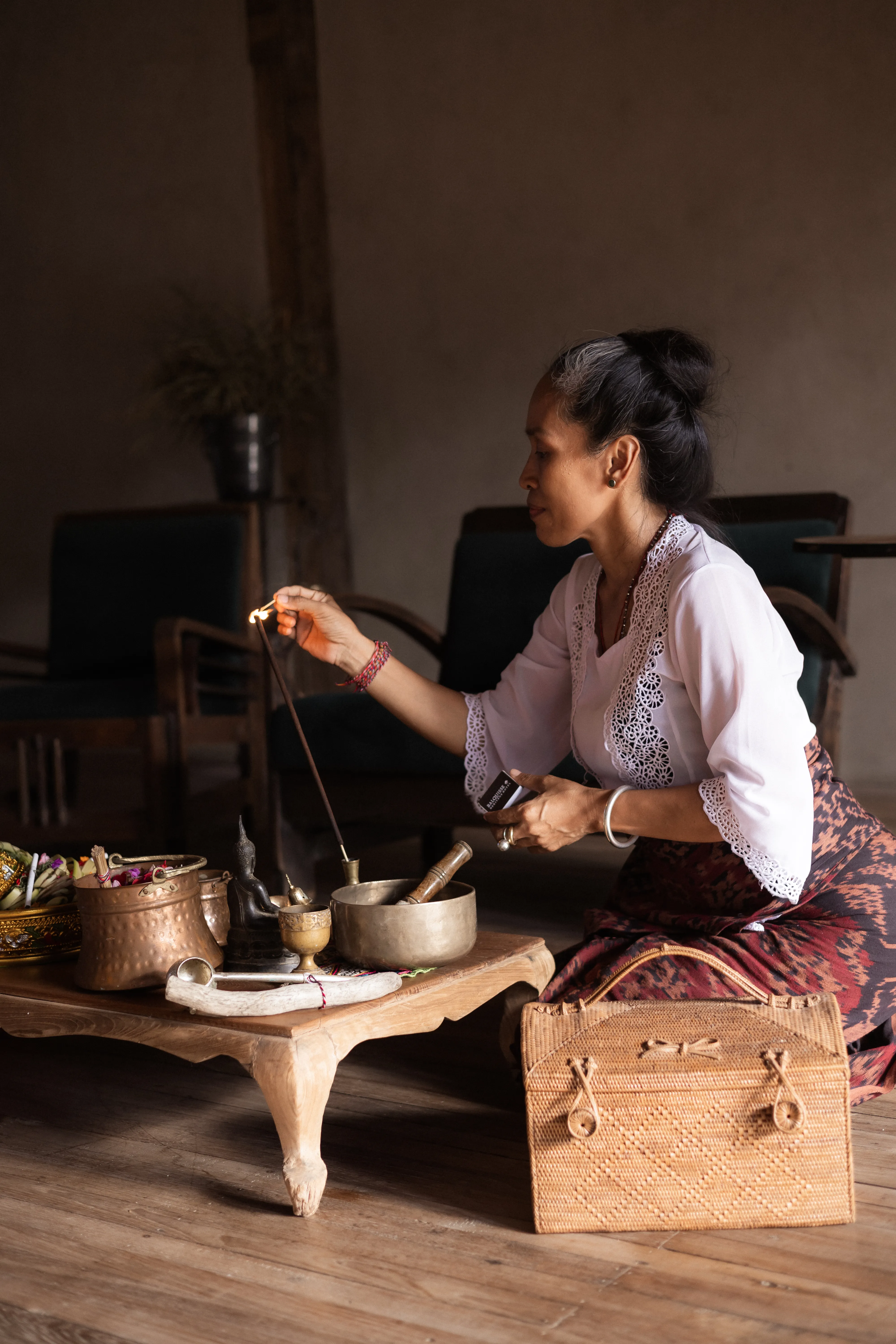 Jero Ani, an esteemed Balinese Balian, lighting incense next to singing bowls and ritual tools during a spiritual guidance session.