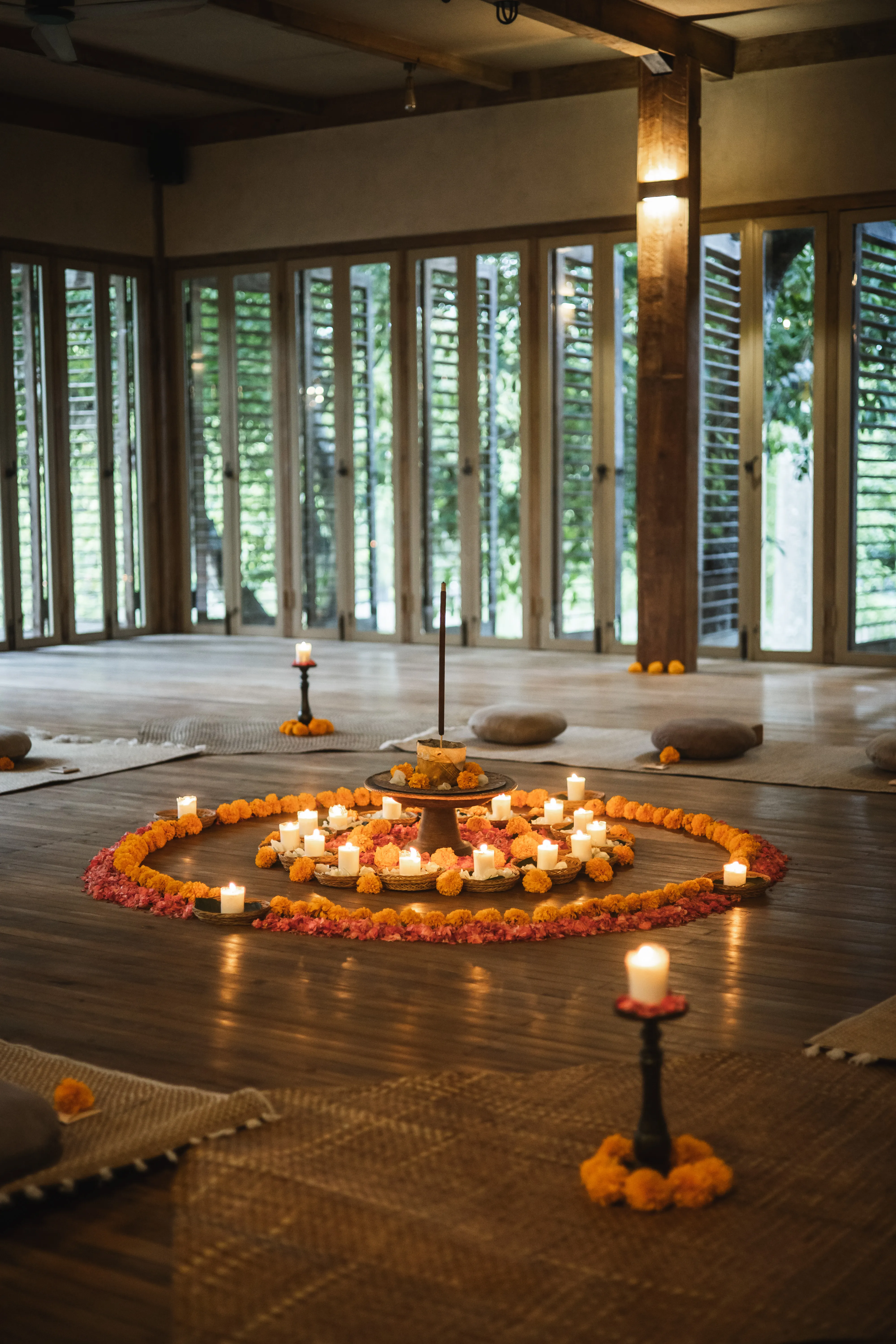 A sacred flower mandala crafted from orange marigolds and pink petals surrounded by burning candles inside a wooden retreat at shaba shala.