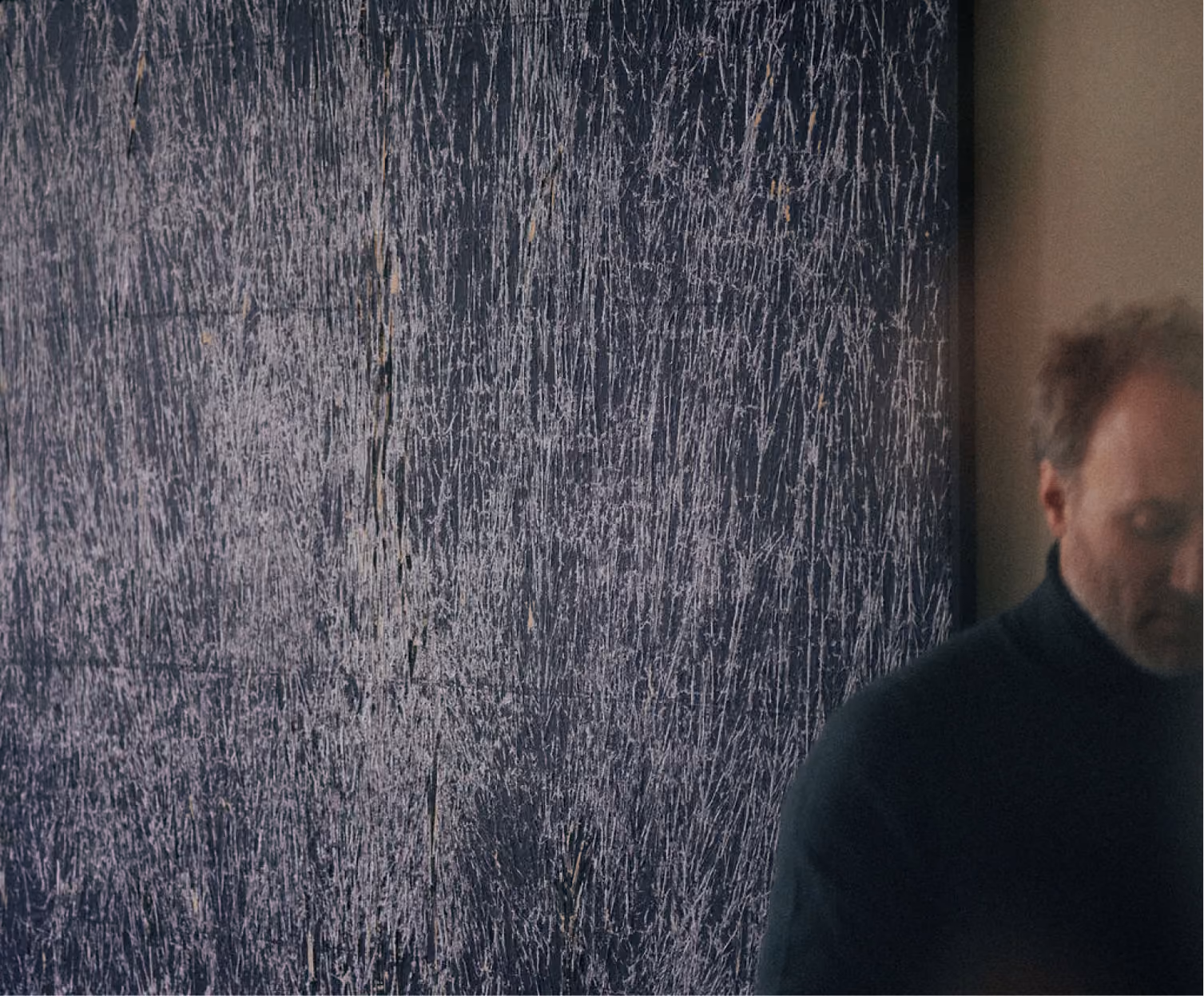 Notaris Matthias Moortgat met een zwarte coltrui staat half zichtbaar rechts van een grote, zwart-witte abstracte schilderij met fijne, willekeurige lijnen aan de muur.