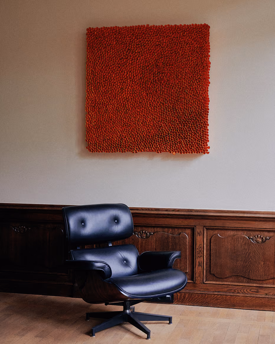 Zwarte lederen fauteuil met houten details staat voor een muur met donkere houten lambrisering en een vierkante rood kunstwerk met textuur erboven. Kunst te zien in het kantoor van Scriptas Notarissen.