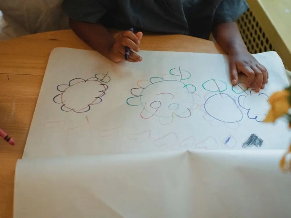 Mani di un bambino che disegnano con i pastelli su un foglio