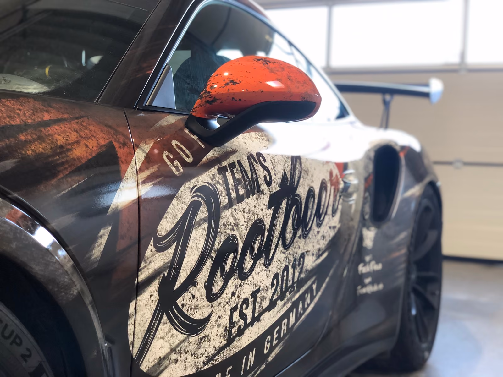 Porsche 911 GT3 RS mit Rost-Design-Folierung, Seitenansicht mit Root-Beer-Schriftzug in der Werkstatt