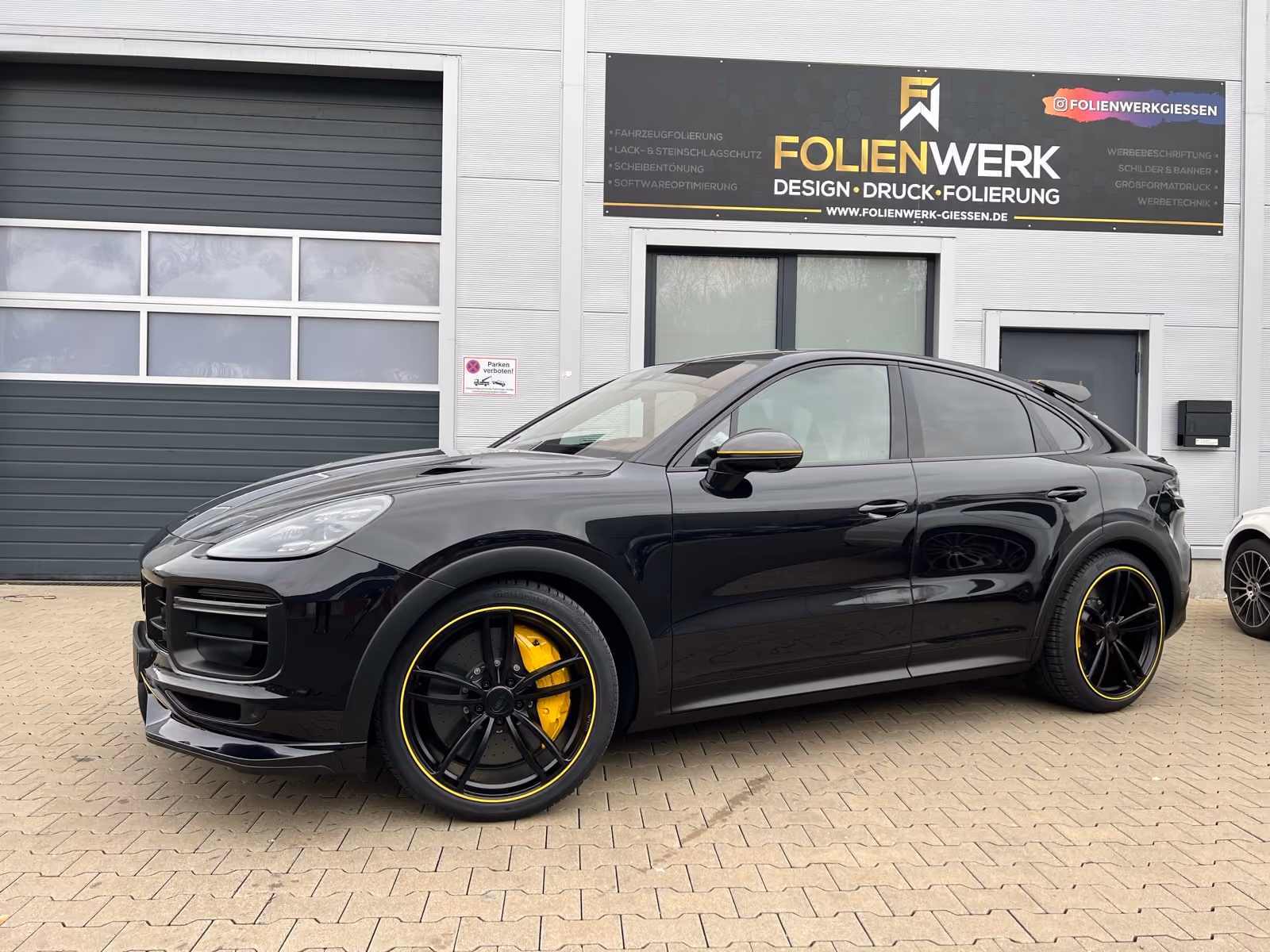 Schwarzer Porsche Cayenne Coupé mit gelben Felgenakzenten nach der Folierung vor dem Folienwerk Gießen