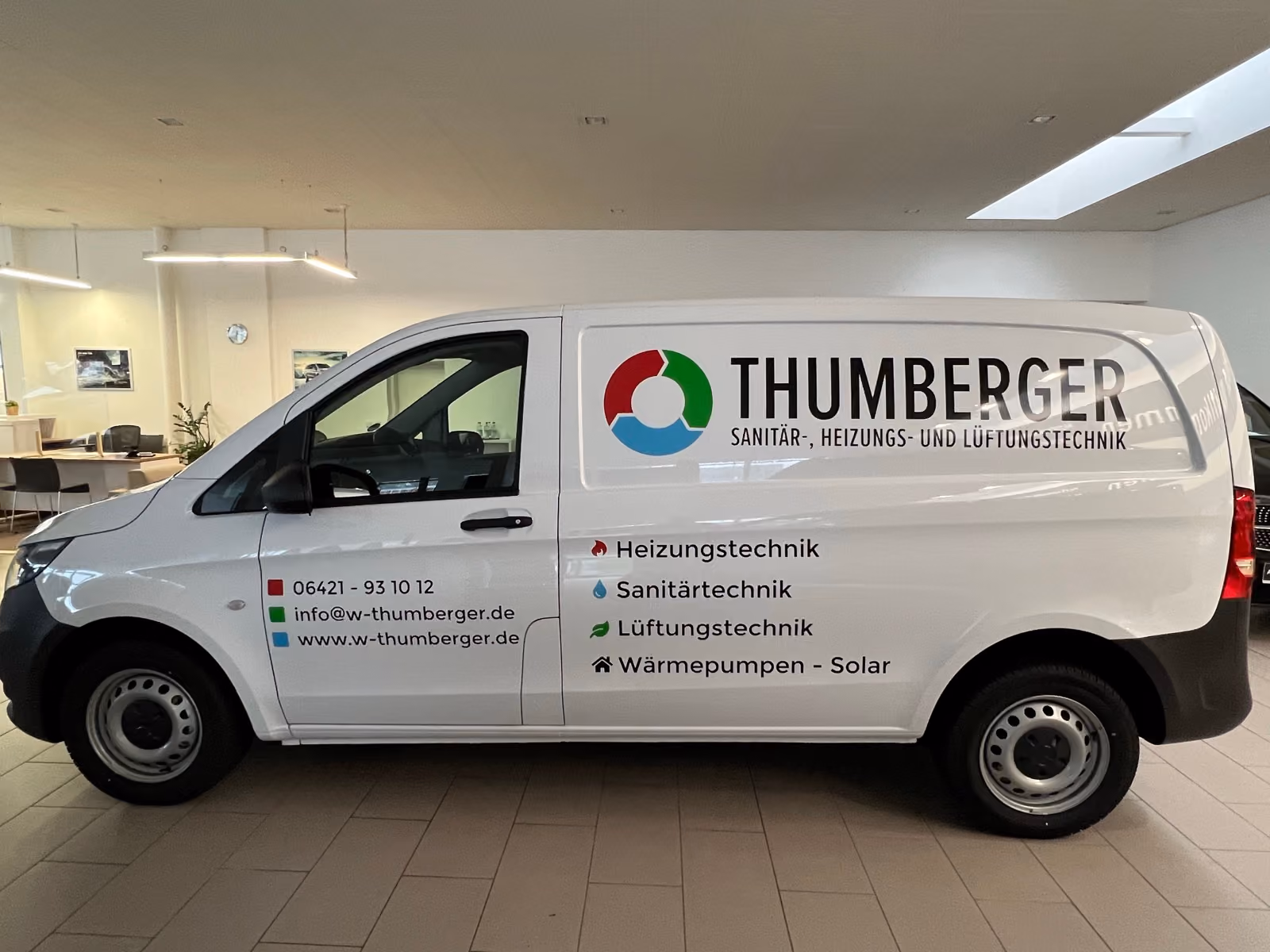 Weißer Mercedes Vito mit Werbebeschriftung für Sanitär-, Heizungs- und Lüftungstechnik im Showroom