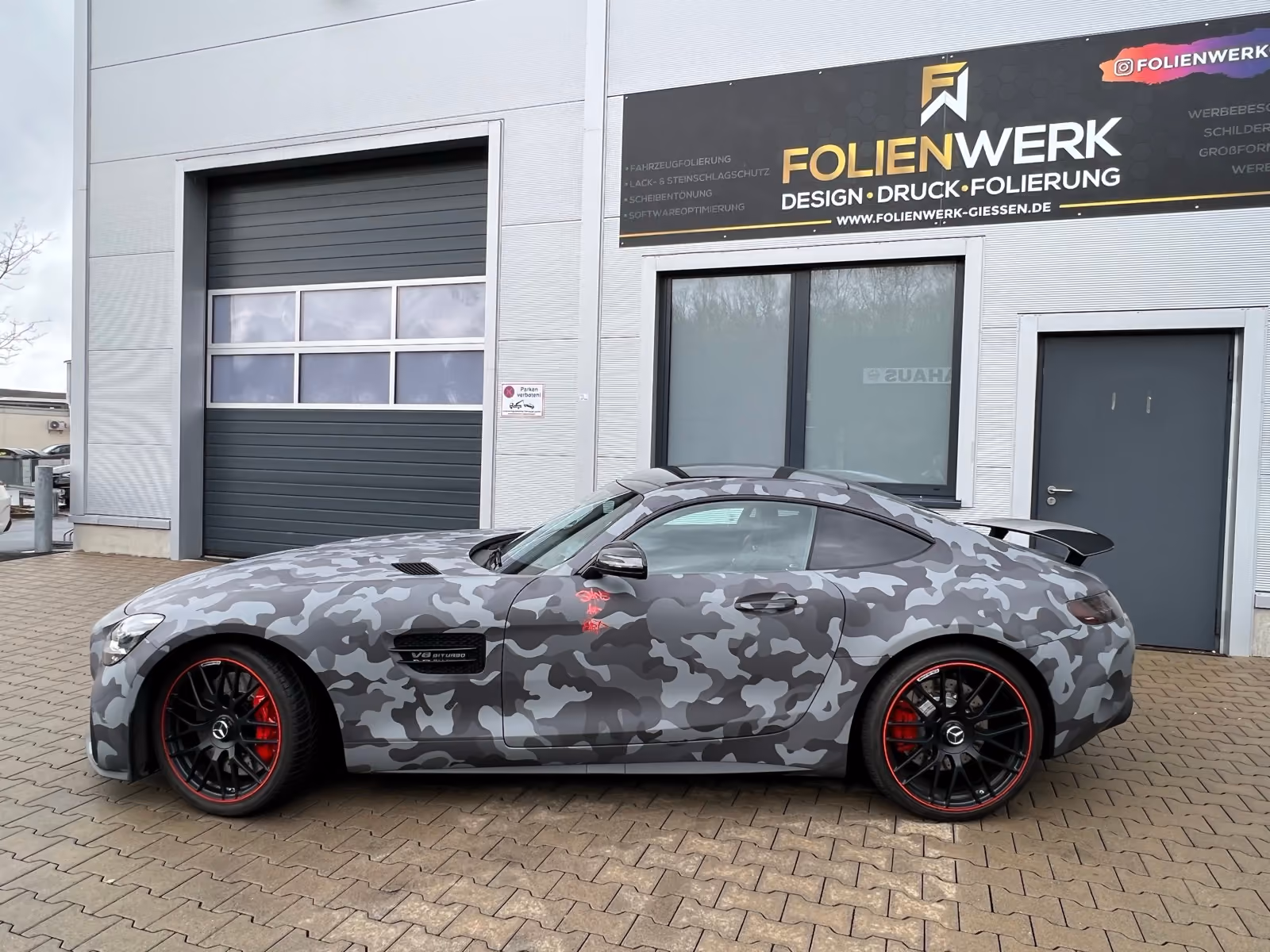 Mercedes-AMG GT mit Camouflage-Folierung in Grautönen vor dem Folienwerk Gießen