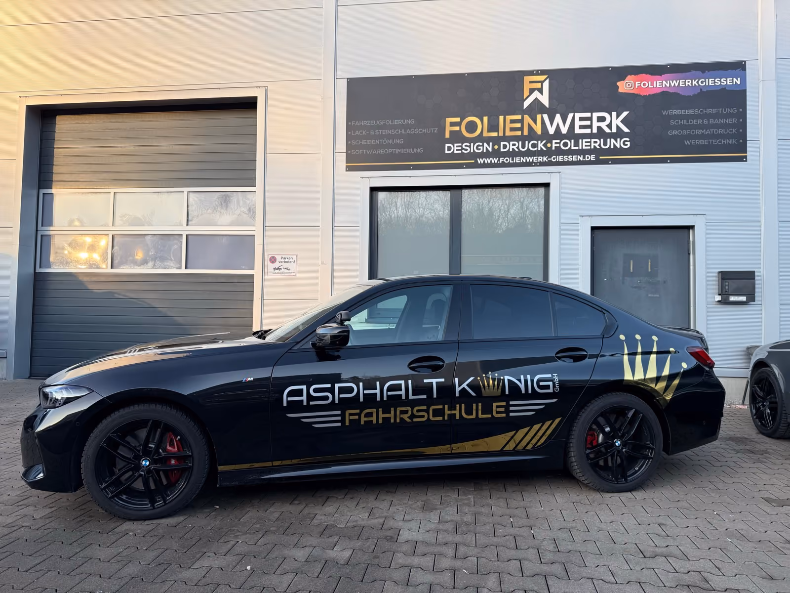 Schwarzer BMW 3er mit goldener Werbebeschriftung einer Fahrschule vor dem Folienwerk Gießen