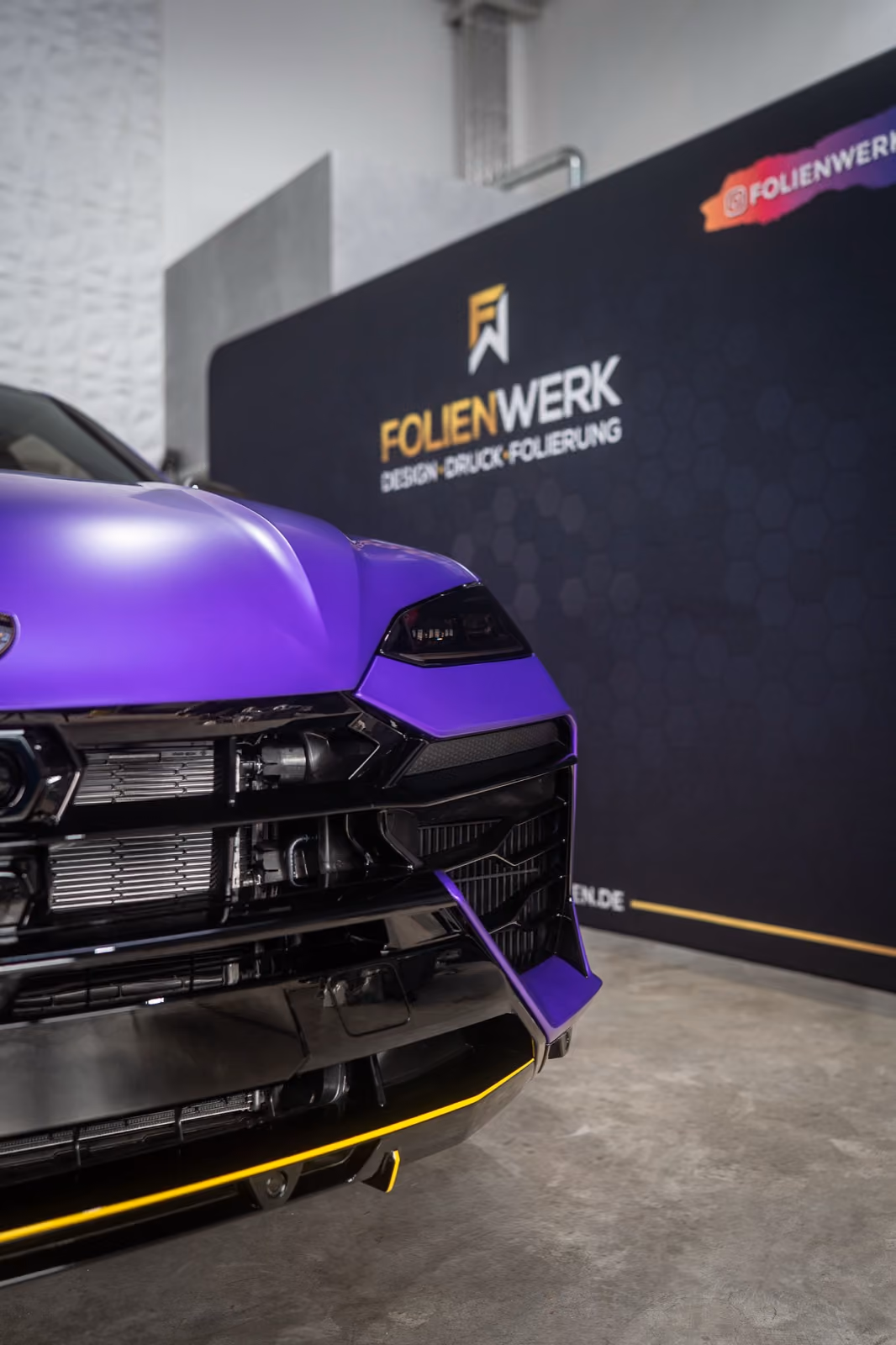 Frontdetail eines mattviolett folierten Lamborghini Urus vor der Logowand des Folienwerk Gießen