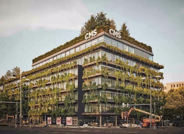 Modern building covered with green plants hanging from balconies and rooftop greenery.