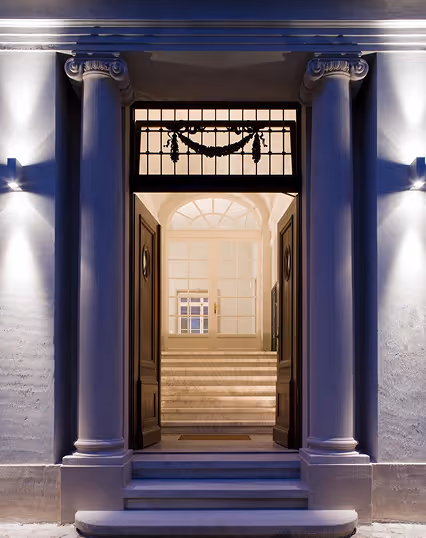 Open doorway framed by two classical columns leading to stairs and a window inside a building at night.